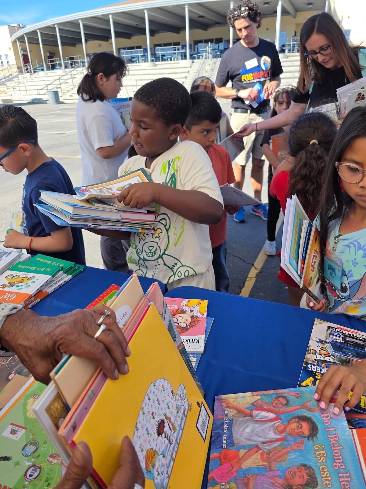 Child stacking books with other children at a book giveaway table during a literacy event with United Way of San Diego County