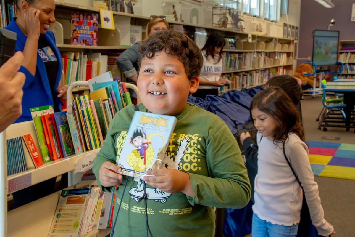 Young boy holding a book and smiling in a library during a book giveaway with United Way of San Diego County