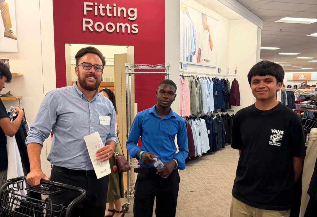 two teens and a volunteer stand in front of a dressing room entrance at Kohl's during a Dream with STEAM shopping event