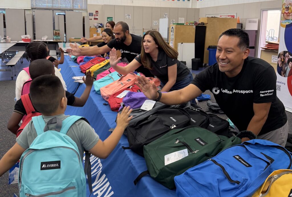 Employees from Collins Aerospace high-five school children during a backpack giveaway event as part of a CSR volunteer opportunity with United Way of San Diego County