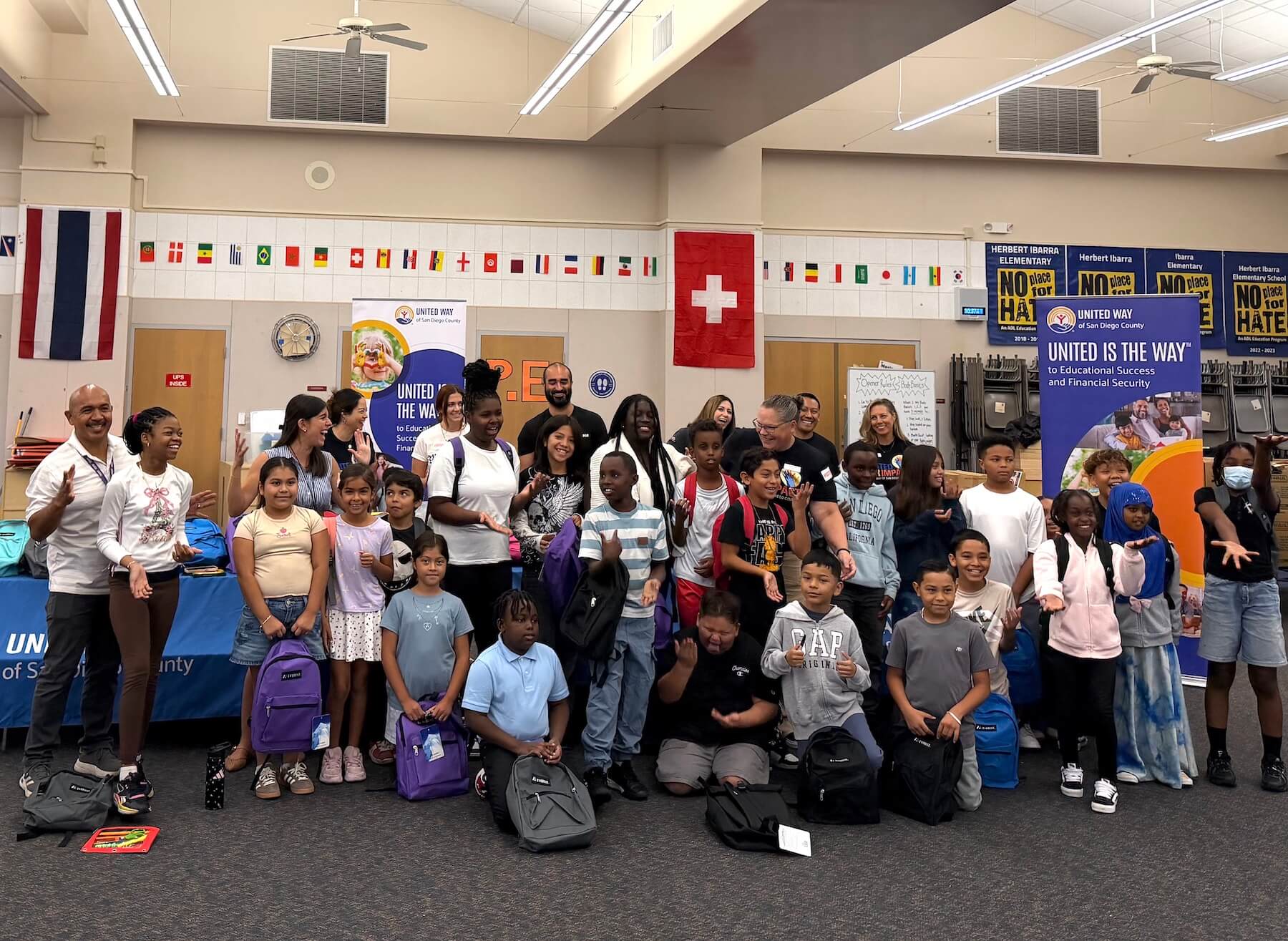 CSR volunteers from Collins Aerospace pose with a group of school children, administrators, and staff from UWSD during a backpack giveaway volunteer event through United Way of San Diego County